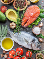 Raw dorado fish and salmon steak with spices and vegetables on the graphite board.
