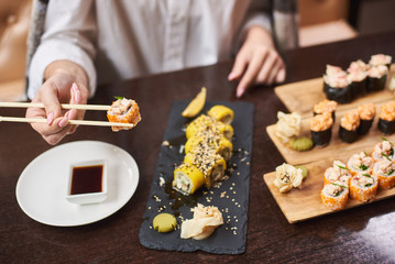 Close-up woman hands with food sticks, traditional Japanese dish with wasabi. Woman eating and enjoying fresh sushi in luxury restaurant. Client holding food sticks and eating oriental meal on lunch