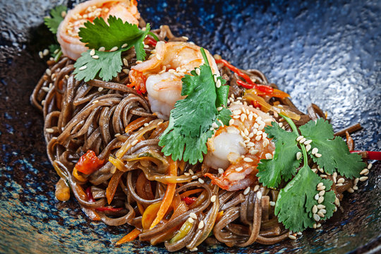 Close up on buckwheat noodles with shrimps served in black textured bowl. Thai cuisine. Seafood. Reaydy for eat. Picture for recipe. Copy space for design. Soba seafood