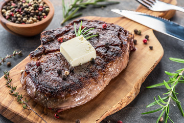 Medium rare Ribeye steak with herbs and a piece of butter on the wooden tray.