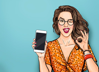 Winking woman in glasses showing smart pone and OK sign. Pop art girl holding phone. Digital advertisement female model showing the message or new app on cellphone. - obrazy, fototapety, plakaty