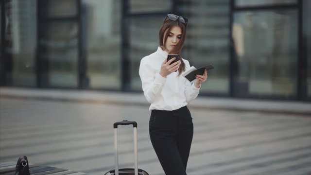 Business woman or attractive girl in a white shirt with luggage checks tickets on mobile phone and passport. Error at online check-in or incorrectly selected seats.Woman check-in online registration