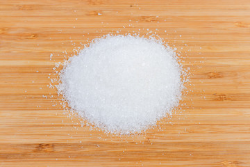 Handful of the white sugar on a wooden surface