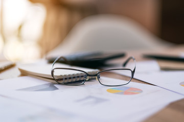 Close up image of black eyeglasses with paperwork on the table