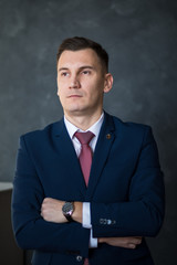 Portrait of young intelligent man lawyer standing with crossed arms in modern office building interior, successful male bank employee dressed in luxury suit posing with copy space area for your text
