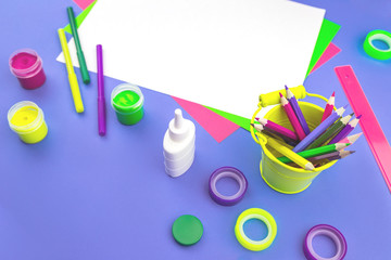 Bright purple violet desk with paper, paint and assorted neon stationery items in top view and selective focus, arts and craft in school education or office and creativity concept. Copy space top view