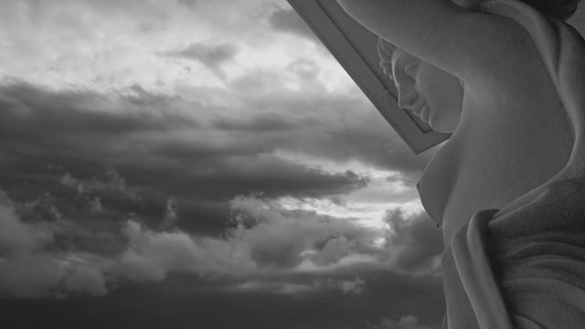 A beautiful french colonial statue of a nymph superimposed on a dramatic time lapse sky in Black and White. The sky changes mood throughout the clip. It has an french impressionist feeling.