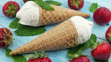 Waffle cones ice cream and strawberries are lying on the blue wooden board