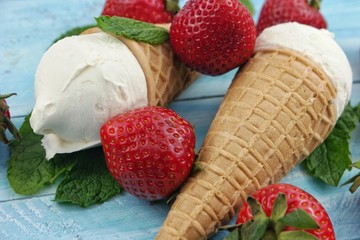 Waffle cones ice cream and strawberries are lying on the blue wooden board