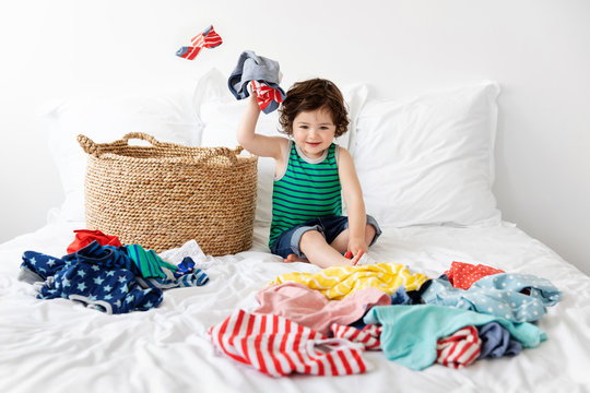 Happy Toddler Sitting Next To Laundry Basket Making Mess With Clothes