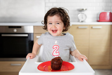 Happy toddler in high chair with cake celebrating second birthday