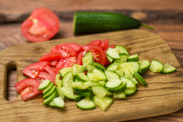 Sliced fresh tomato and cucumber on a wooden board. Cooking vegetable salad. The concept of healthy, vegan food.