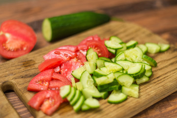 Sliced fresh tomato and cucumber on a wooden board. Cooking vegetable salad. The concept of healthy, vegan food.