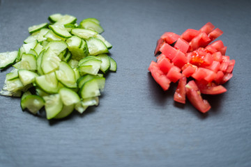 Sliced fresh cucumbers and tomatoes on a black background. Cooking salad from vegetables. The concept of healthy eating, vegetarianism.