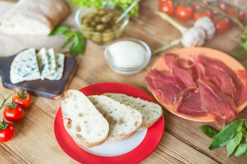 Ingredients for cooking bruschetta: chopped ciabatta, olives, tomatoes, blue cheese, jamon on a wooden background. Cooking healthy and tasty food.