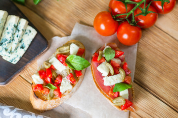 Traditional Italian bruschetta with blue cheese, feta, tomatoes, basil leaves, jamon on a wooden background.