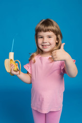 girl child in pink clothes holding a banana with a cocktail tube in his hand, the other hand shows...