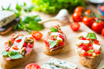 Traditional Italian bruschetta with blue cheese, feta, tomatoes, basil leaves, jamon on a wooden background.