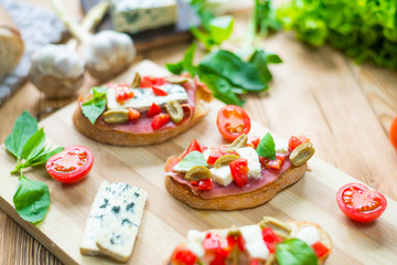 Fototapeta na wymiar Traditional Italian bruschetta with blue cheese, feta, tomatoes, basil leaves, jamon on a wooden background.