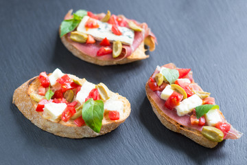 Traditional Italian bruschetta with blue cheese, feta, tomatoes, basil leaves, jamon on black stone background.