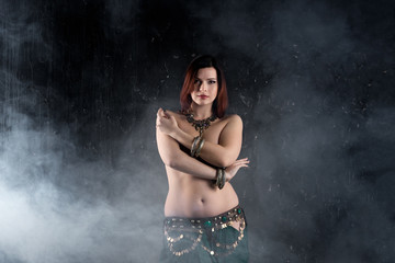 Fototapeta premium Sexy women performs belly dance in ethnic dress on dark smoky background, abstract art photography