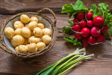 Fresh raw organic vegetables: potatoes, radishes, green onions on a wooden background.