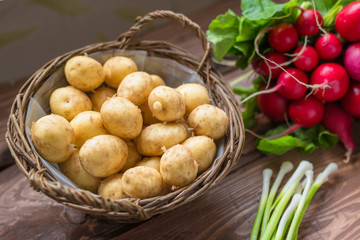 Fresh raw organic vegetables: potatoes, radishes, green onions on a wooden background.