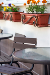 Glass and metal tables and chairs on a summer terrace cafe by the window with pots of flowers