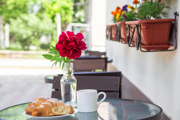 Two croissants on a plate next to a cup of cappuccino on a street table of a summer terrace cafe. Beautiful breakfast outdoor