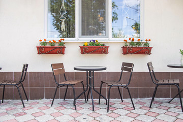 Glass and metal tables and chairs on a summer terrace cafe by the window with pots of flowers