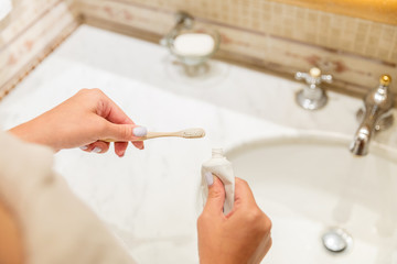 Cropped image of attractive woman hand applying toothpaste on toothbrush in bathroom. Beauty healty wellness morning concept