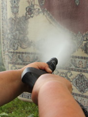 Woman hands cleaning the carpet outside with a high-pressure water wash