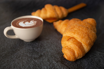 freshly baked croissants on a black background with a white coffee cup,breakfast bread brown...