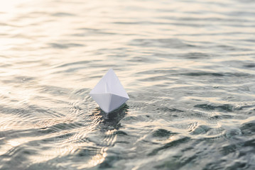 Alone paper boat floats on the water at sunset.