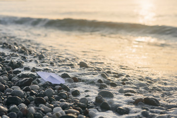 Paper boat lies on the seafront at sunrise.