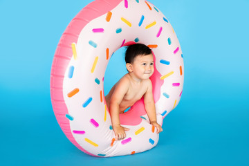 Cute little baby boy in inflated rubber ring on blue colour background