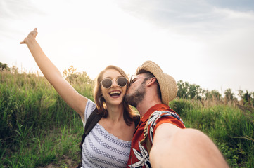 Romantic couple taking a selfie and kissing on a field at vacation