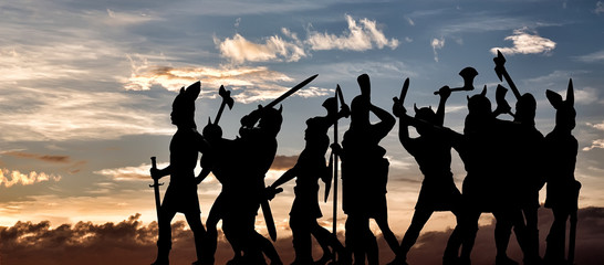 Group of attacking Vikings (silhouettes of vintage toy soldiers) against sunset sky with clouds, Old Norse, Odin, Asgard and Valhalla themes - obrazy, fototapety, plakaty