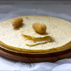 A stack of round corn tortillas on a wooden board and corncobs.