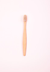 Top view of bamboo toothbrush on pastel pink background. Plastic free concept.