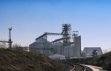 Fototapeta na wymiar View of modern sugar factory with industrial silos (large metal tanks for sugar, grain or silage storage), buildings, towers and other metal structures and equipment, blue sky background
