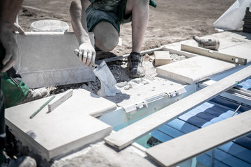 Gartenbauer setzt Steinplatte und streicht den Untergrund mit Fließenkleber ein und richtet die Platte mit dem Hammer aus