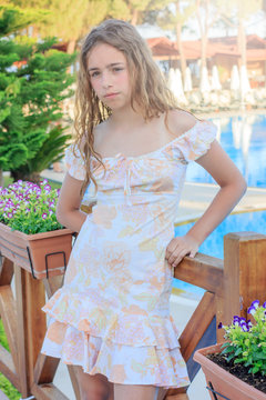 Cute teen girl in a romantic dress and with long hair is standing on the bridge by the pool