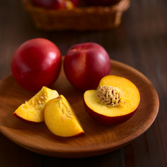 Fresh ripe nectarine fruits cut and whole on wooden plate, photographed on dark wood with natural...