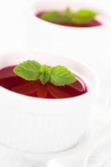 Rote Götterspeise oder Wackelpudding in weißer Schüssel mit Minzblatt garniert (Selektiver Fokus, Fokus auf die Enden der Minzblätter)