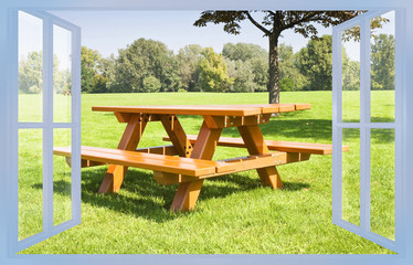 Wooden new picnic table on a green meadow of a public park with trees on background - concept image