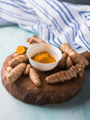 Turmeric spice in powder and roots on wooden board