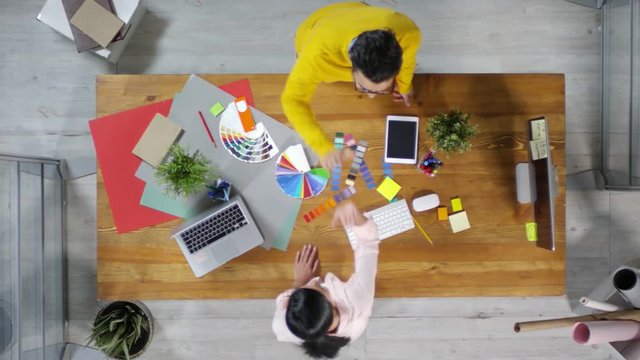 Directly above view of two Middle Eastern interior designers standing at wooden table in front of each other and giving high five