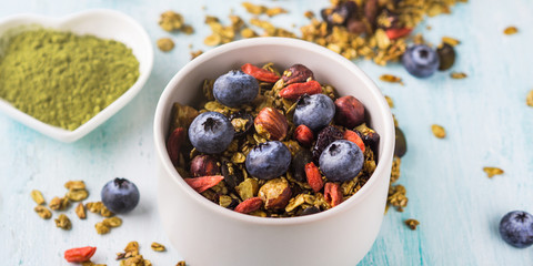 Home made matcha green tea granola in bowl on pastel turquoise background. Oats granola with goji berries, dried fruit, seeds and nuts. Healthy breakfast concept