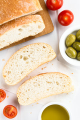 Frisches italienisches Ciabatta Brot in Scheiben geschnitten, Kirschtomaten, Oliven und Olivenöl an der Seite (Selektiver Fokus, Fokus auf die Brotscheiben)